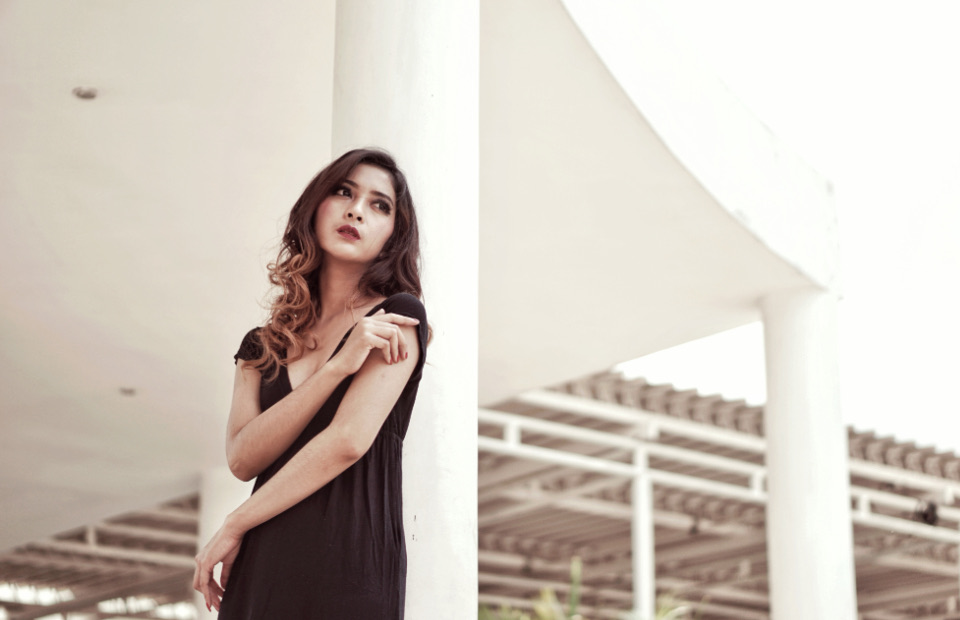 ผู้หญิงใส่เดรสสีเข้มยืนข้างเสาสีขาว