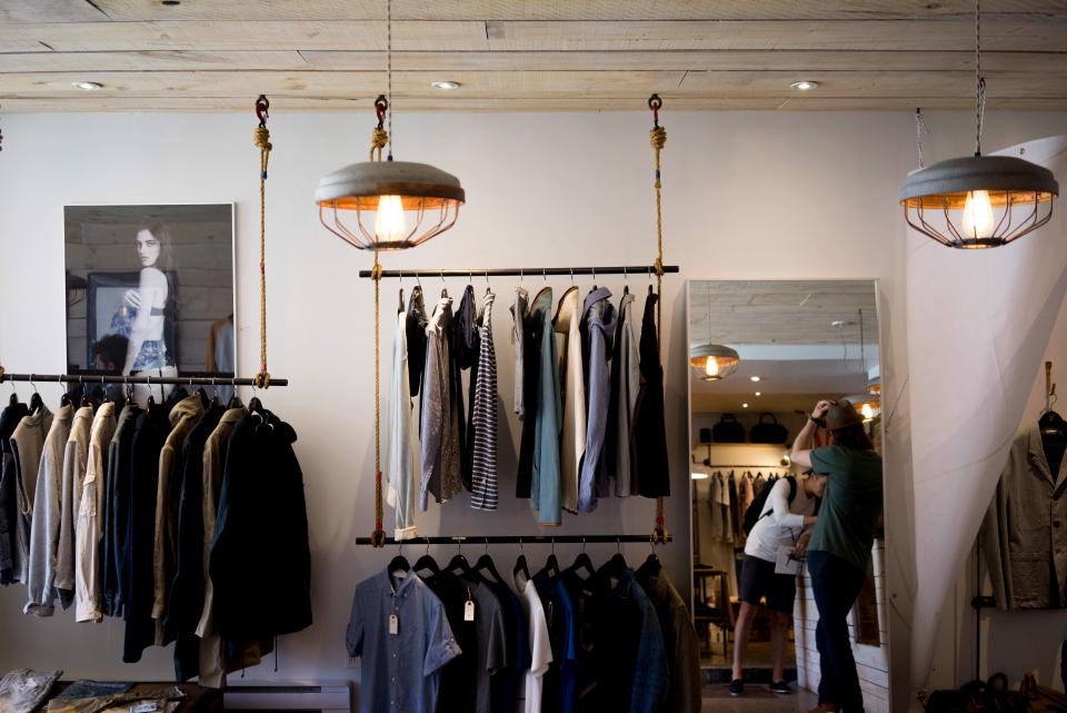 ร้านเสื้อผ้าโทนสว่าง มีราวแขวนเสื้อและโคมไฟ